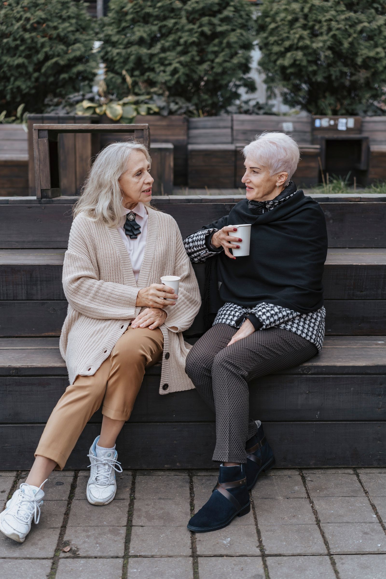 Two women talking together over coffee on a bench outdoors