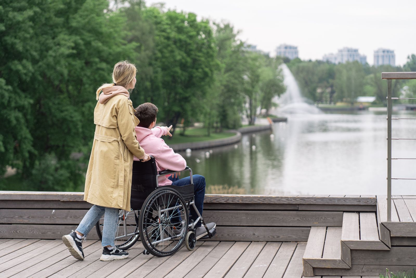 A support worker walking beside a person using a wheelchair along a riverside path